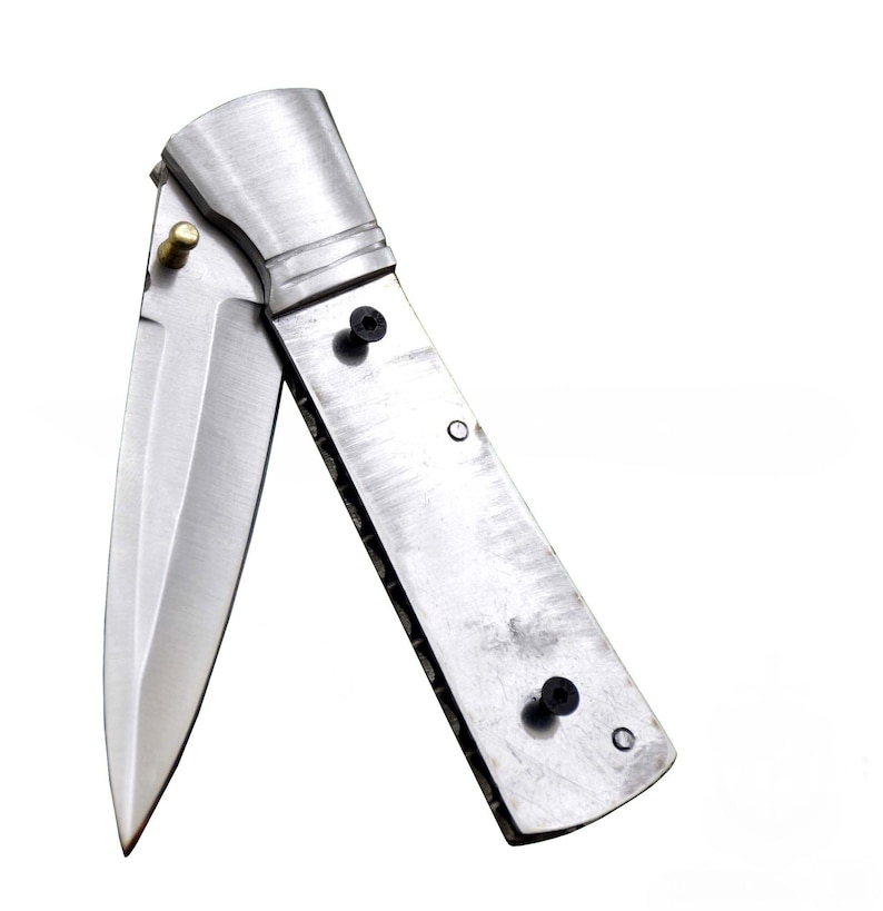 May include: A stainless steel folding knife with a partially open blade. The knife has a brushed metal finish and is set against a white background. The handle is riveted and has a textured edge.