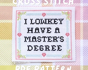 May include: A white fabric square featuring a cross stitch design with the black text I LOWKEY HAVE A MASTER'S DEGREE. The text is framed by a border of light blue and pink stitches with small hearts and floral corner accents on a plaid background.