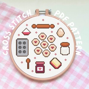 May include: A cross-stitch PDF pattern in a round hoop. The design features baking-related icons, including a rolling pin, cookies, an egg, a jar of jam, and a baking sheet. The text "CROSS STITCH PDF PATTERN" is displayed around the hoop.