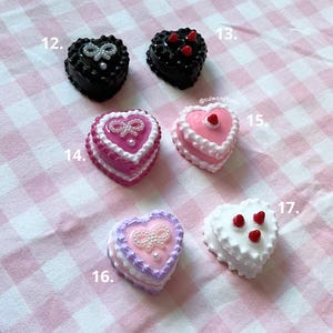 以下が含まれることがあります： ピンク、パープル、ホワイト、ブラックなど、さまざまな色のハート型のケーキチャームの詰め合わせ。一部のチャームには、ホワイトフロスティング、レッドチェリー、ホワイトボウが付いています。チャームは12から17まで番号が付けられています。