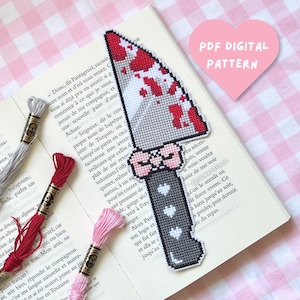 May include: A cross-stitch pattern of a knife with a grey blade featuring red blood-like splatters, a pink bow at the hilt, and a dark grey handle decorated with white hearts. The text PDF DIGITAL PATTERN is visible in a pink heart shape.