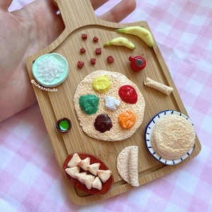 May include: A wooden cutting board with a variety of Indian food items, including a dosa with different toppings, samosas, and a bowl of rice. The board is decorated with red and green accents.