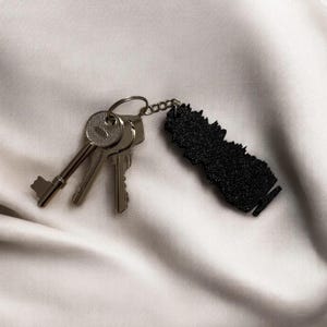 May include: A silver key chain with three keys and a black keychain charm shaped like a city skyline.