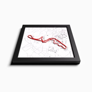 Puede incluir: Un mapa enmarcado de un circuito de carreras con una línea de circuito de carreras roja. El mapa está en un marco negro con un fondo blanco.