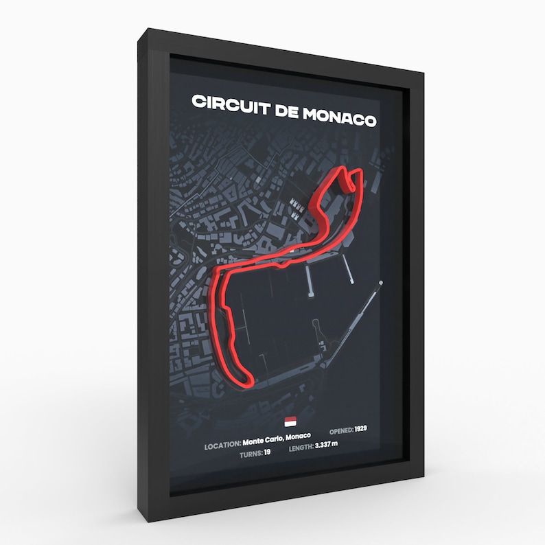 May include: A black framed print of the Circuit de Monaco race track. The track is outlined in red on a dark gray map with the text "CIRCUIT DE MONACO" at the top. The text "OPENED: 1829", "LOCATION: Monte Carlo, Monaco", "TURNS: 19", and "LENGTH: 3.337 m" is at the bottom of the print.