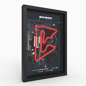 May include: A black framed print of the Bahrain International Circuit race track. The track is outlined in red on a black and white map. The text "BAHRAIN" is at the top of the print. The text "LOCATION: As-Sachir, BAHRAIN", "TURNS: 23", "OPENED: 2004", and "LENGTH: 6.299 m" is at the bottom of the print.