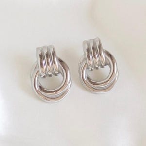 May include: A pair of silver knot-shaped earrings. The earrings are made of a thick, twisted metal.