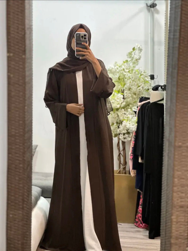 Op de afbeelding: Een bruine abaya met lange mouwen en een vloeiende silhouet. De abaya wordt gedragen over een wit onderhemd.