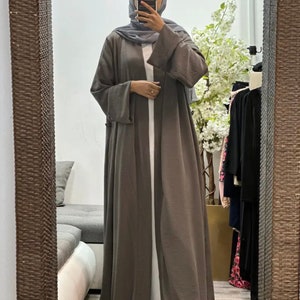 Op de afbeelding: Een lange, losse, grijze cardigan met lange mouwen en een shawlkraag. De cardigan is open aan de voorkant en heeft een vloeiende silhouet.