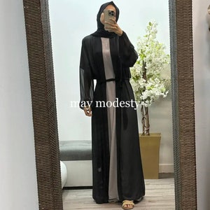 May include: A black sheer long-sleeved cardigan with a tie belt. The cardigan is worn over a long-sleeved dress. The text "may modesty" is visible on the bottom of the image.