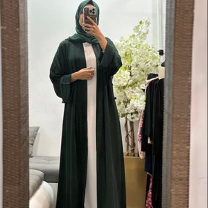 Op de afbeelding: Een lange, donkergroene abaya met lange mouwen en een wit onderhemd. De abaya is gemaakt van een zachte, vloeiende stof.