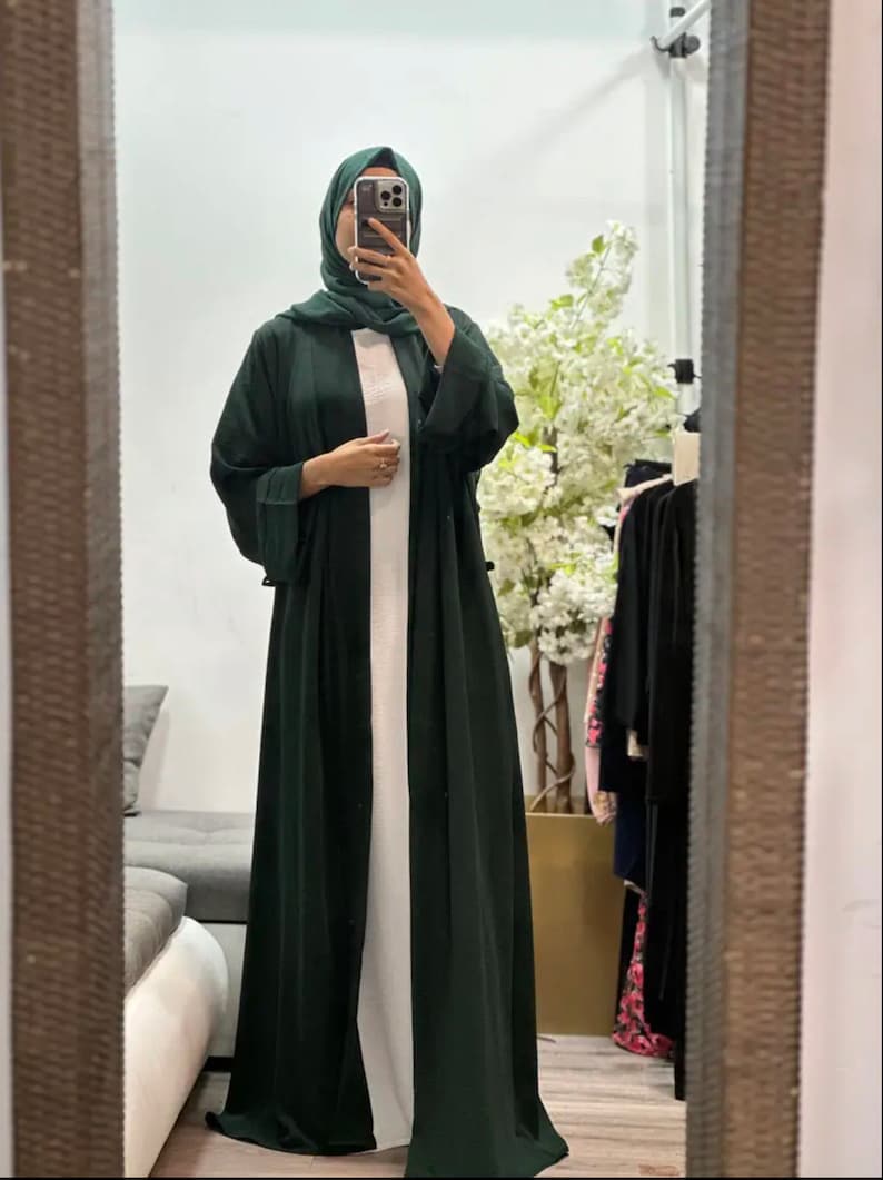 Op de afbeelding: Een lange, donkergroene abaya met lange mouwen en een wit onderhemd. De abaya is gemaakt van een zachte, vloeiende stof.