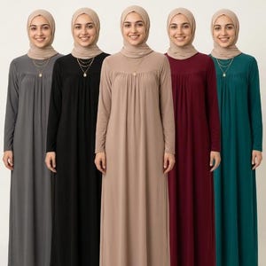 May include: Five long-sleeved maxi dresses in grey, black, beige, burgundy, and teal. Each dress features a round neckline with subtle vertical pleats at the chest and a simple, flowing silhouette. Each dress is paired with a matching headscarf.