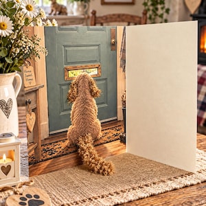 Könnte beinhalten: Eine Grußkarte mit einem lockigen braunen Hund, der auf einer Fußmatte sitzt und durch den Briefschlitz einer salbeigrünen Tür schaut. Die Karte ist aufgeklappt, zeigt eine leere Innenseite und steht auf einer hölzernen Oberfläche mit Dekoration.
