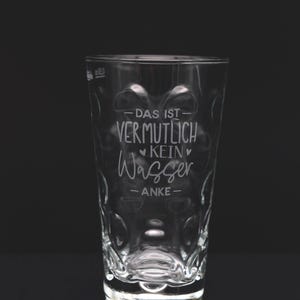 Könnte beinhalten: Ein klares Glas mit strukturiertem Design und dem deutschen Text "DAS IST VERMUTLICH KEIN Wasser -ANKE-" auf der Vorderseite. Das Glas steht vor einem schwarzen Hintergrund.