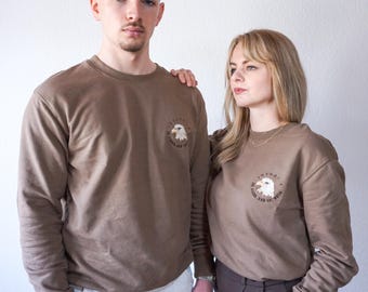 May include: Two people wearing brown sweatshirts with an embroidered eagle design and the text "Forward" in a circle around the eagle. The text below the eagle says "Fly High And See The World".