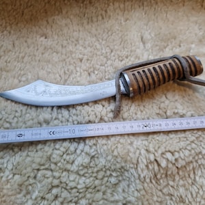 Könnte beinhalten: Ein gebogenes, silbernes Messer mit einem Holzgriff und einem Lederriemen. Die Klinge ist mit dem Text "FLEINFICIEL" graviert. Das Messer ist 30 cm lang.