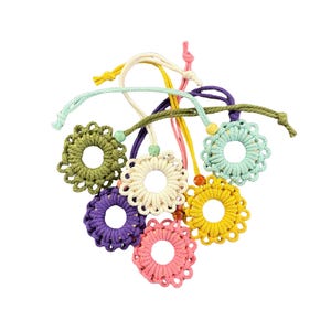 May include: A selection of colourful, crocheted flower ornaments in shades of green, purple, pink, yellow, and cream. Each flower has a central hole and is attached to a matching cord with a bead. The cords are in various colours.