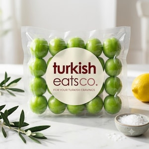 Può includere: Una confezione quadrata in plastica sottovuoto contenente quindici prugne verde brillante disposte a griglia. Un'etichetta circolare bianca al centro presenta il testo rosso scuro "turkish eats co." e "FOR YOUR TURKISH CRAVINGS" in caratteri più piccoli.