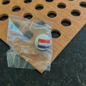 May include: A white marble with a red, white, and blue flag design. The marble is in a clear plastic bag on a wooden surface.