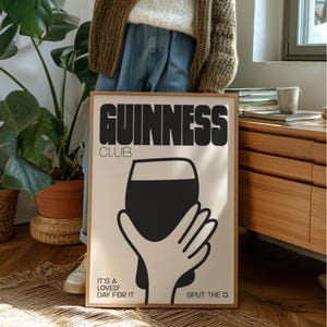 Pu&ograve; includere: Un poster incorniciato con la scritta "GUINNESS CLUB" in nero. Il poster mostra una pinta nera di Guinness tenuta da una mano. Sono incluse anche le frasi "IT'S A LOVELY DAY FOR IT" e "SPLIT THE Q."