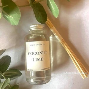 Può includere: Una bottiglia di vetro trasparente con un tappo argentato riempita di un liquido trasparente. La bottiglia ha un'etichetta bianca con il testo "Mecha Candle Co. Coconut Lime Reed Diffuser 3.5 fl oz/100g".