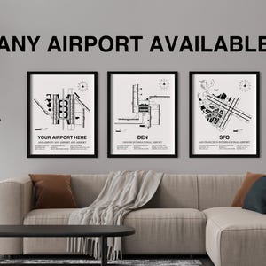 May include: Three black and white framed prints of airport layouts. The prints are hanging on a gray wall above a light gray couch. The prints feature the text "Your Airport Here", "DEN", and "SFO".