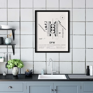 May include: Black and white print of the Dallas Fort Worth International Airport layout, with the text "DFW" and "Dallas Fort Worth International Airport" below the map. The print is framed in black and hanging on a white tiled wall in a kitchen.