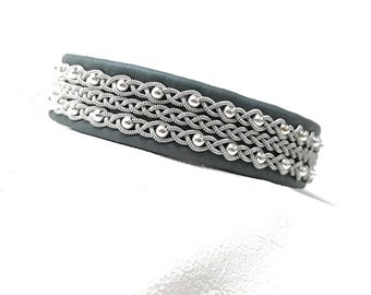 May include: A dark gray headband with three rows of silver-colored, woven metal detailing. The metalwork features a repeating pattern of interwoven strands and small, round beads. The headband is set against a white background.