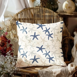 May include: A white cushion with a blue and beige starfish pattern. The cushion is sitting on a wicker chair.