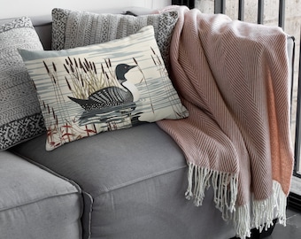 Könnte beinhalten: Ein graues Sofa mit einer rosa-weißen gestreiften Wolldecke und einem Kissen mit einem Motiv eines Seetaucher und Schilfs.