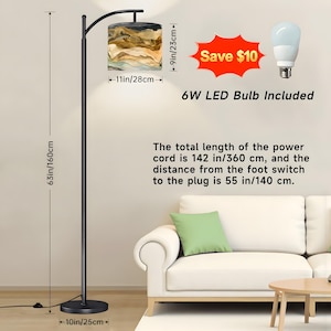 May include: A black floor lamp with a lampshade featuring a beige and brown abstract design. The lamp is 63 inches (160 cm) tall, with a 10-inch (25 cm) base and a lampshade that is 11 inches (28 cm) wide and 9 inches (23 cm) tall. Includes a 6W LED bulb.