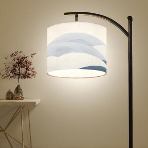 May include: A modern floor lamp with a black metal frame and a cylindrical lampshade. The lampshade features a white background with a blue wave design. The lamp is next to a small table with a vase of flowers.