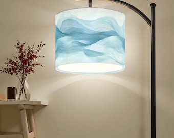 May include: A floor lamp with a black metal frame and a cylindrical lampshade. The lampshade features a light blue and white wavy pattern. A small table with a vase of red flowers and a candle sits to the left of the lamp.