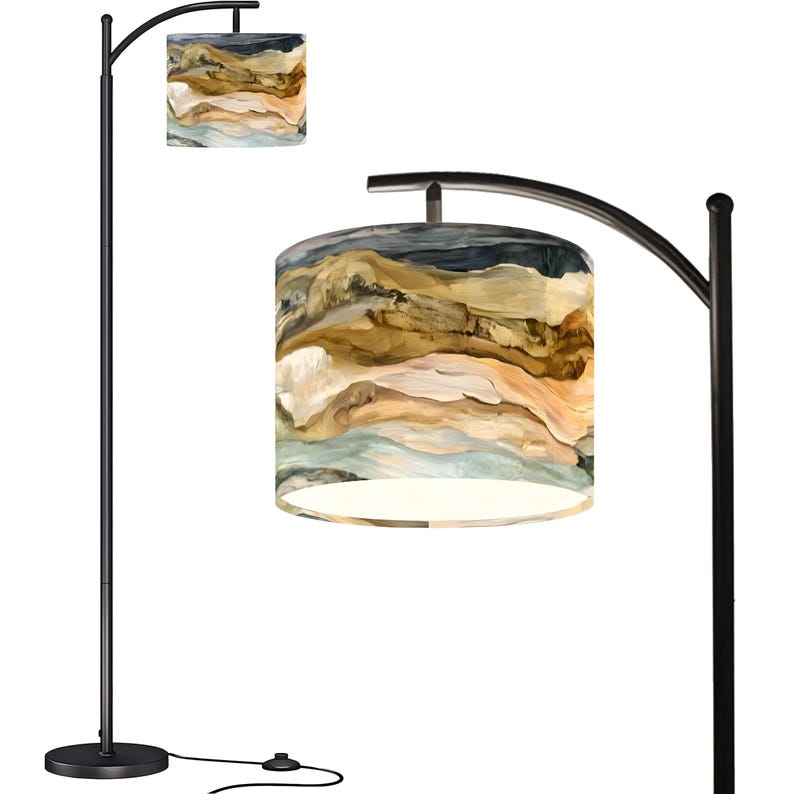 May include: A black arc floor lamp with two lampshades. The lampshades feature a landscape design in shades of brown, beige, and blue. The lamp has a round base and a curved arm.