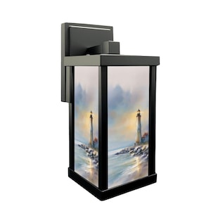 May include: Black outdoor wall-mounted lantern with a rectangular shape. The lantern features a painted scene of a lighthouse on the ocean. The artwork is visible through the glass panels of the lantern.