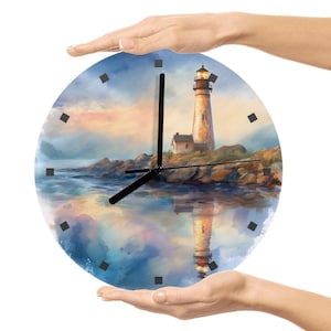 May include: Round wall clock featuring a lighthouse scene with a coastal landscape. The clock face has a painted image of a lighthouse on a rocky shore, with a reflection in the water. Black clock hands and square hour markers.