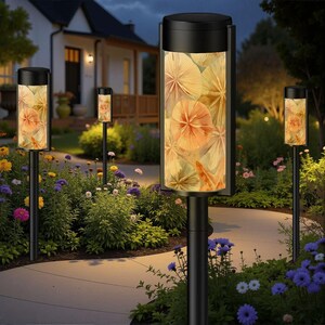 May include: Outdoor pathway lights with a black finish and cylindrical shades. The shades display a floral pattern in shades of orange and yellow. The lights are installed along a curved walkway in a garden with colorful flowers.