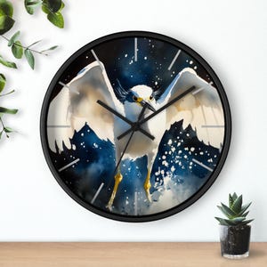 Puede incluir: Un reloj de pared negro con un diseño de acuarela de un pájaro blanco con acentos azules y amarillos sobre un fondo azul oscuro con motas blancas.
