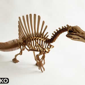 Könnte beinhalten: Ein Holzmodell eines Spinosaurus-Skeletts, ein großer theropoder Dinosaurier mit einem markanten Segel auf dem Rücken. Das Modell ist zusammengebaut und in einer Gehposition aufgestellt. Das Modell ist aus Naturholz gefertigt und hat eine hellbraune Farbe.