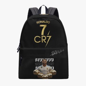 May include: A black backpack featuring the gold text RONALDO, the number 7, and CR7. The front pocket displays a white signature, a photographic print of Cristiano Ronaldo in a white jersey, the text SIUUU, and five gold soccer balls at the base.