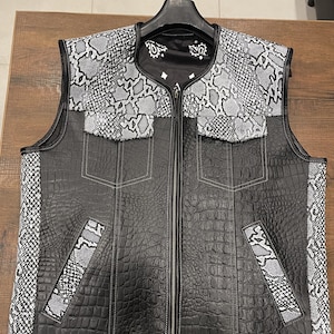 May include: A black leather vest with a zip fastening. The vest has a crocodile-embossed pattern and is accented with white snake skin panels.