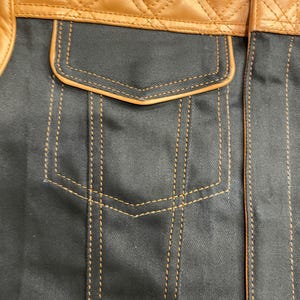 Puede incluir: Primer plano de una chaqueta con una secci&oacute;n superior de cuero marr&oacute;n acolchado y un cuerpo de tela gris oscuro. La chaqueta tiene un bolsillo con ribete marr&oacute;n y detalles de costura dorados.
