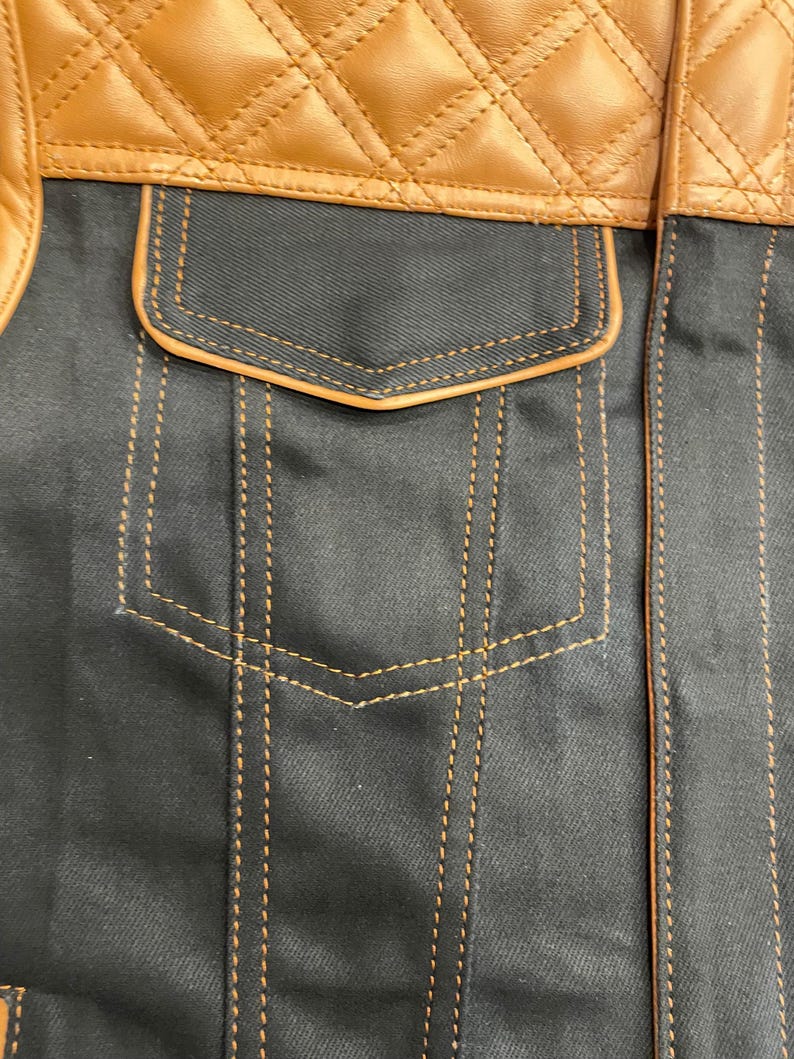 Puede incluir: Primer plano de una chaqueta con una secci&oacute;n superior de cuero marr&oacute;n acolchado y un cuerpo de tela gris oscuro. La chaqueta tiene un bolsillo con ribete marr&oacute;n y detalles de costura dorados.