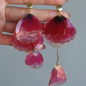 May include: A pair of dangle earrings with multiple layers of pink and white resin flower petals, each petal outlined in gold wire. The earrings have gold hooks.