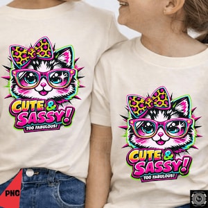 May include: Two cream-coloured t-shirts featuring a cartoon cat wearing glasses and a bow. The cat design is pink and black, with the words "CUTE & SASSY! TOO FABULOUS!" in a vibrant font.