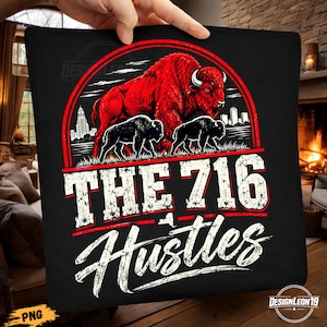 May include: A black t-shirt featuring a graphic of a large red bison standing over two smaller black bison. The design includes a city skyline, a red circular border, and the white text "THE 716 HUSTLES" with a small outline of New York state.