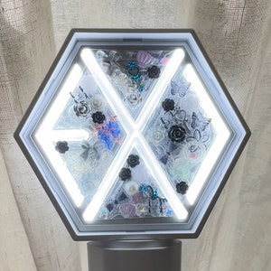 Puede incluir: Un bastón de luz hexagonal blanco y gris con un interior decorativo. El interior presenta rosas blancas y negras, mariposas y otros adornos. El bastón de luz tiene un mango blanco y una luz brillante y brillante.