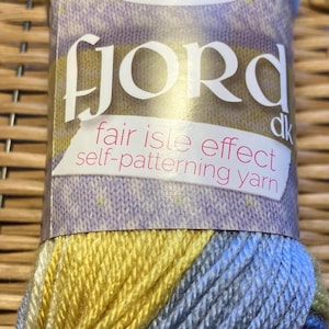 May include: A skein of King Cole Fjord dk yarn in shades of yellow, blue, and gray. The label reads "Fjord" and "fair isle effect self-patterning yarn."