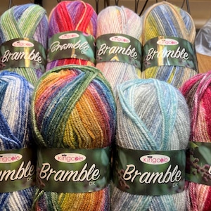 以下が含まれることがあります： さまざまな色の毛糸の束のコレクション。各束には「Bramble DK」と「kingcole」と書かれた緑色のラベルが付いています。毛糸の色には、青、緑、赤、紫、黄色が含まれます。毛糸は整然と配置されています。